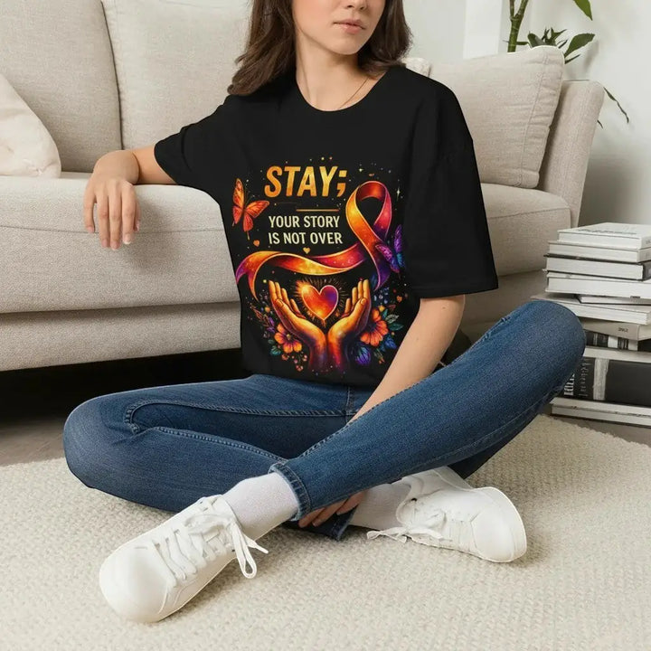 KlareAnsage schwarzes Baumwoll-T-Shirt mit buntem Your Story Is Not Over Aufdruck, getragen von einer Frau auf dem Sofa