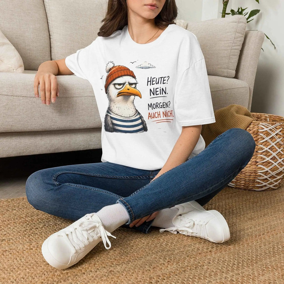 Frau sitzt locker auf dem Boden vor einem Sofa und trägt das weiße Damen-Möwen-Shirt mit Jeans und Sneakers.