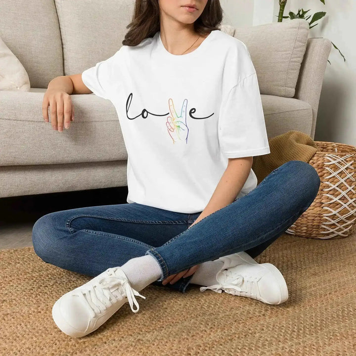 KlareAnsage weißes Gildan 64000 T-Shirt mit Love-Schriftzug und Peace-Hand im Regenbogen-Design an einer sitzenden Frau